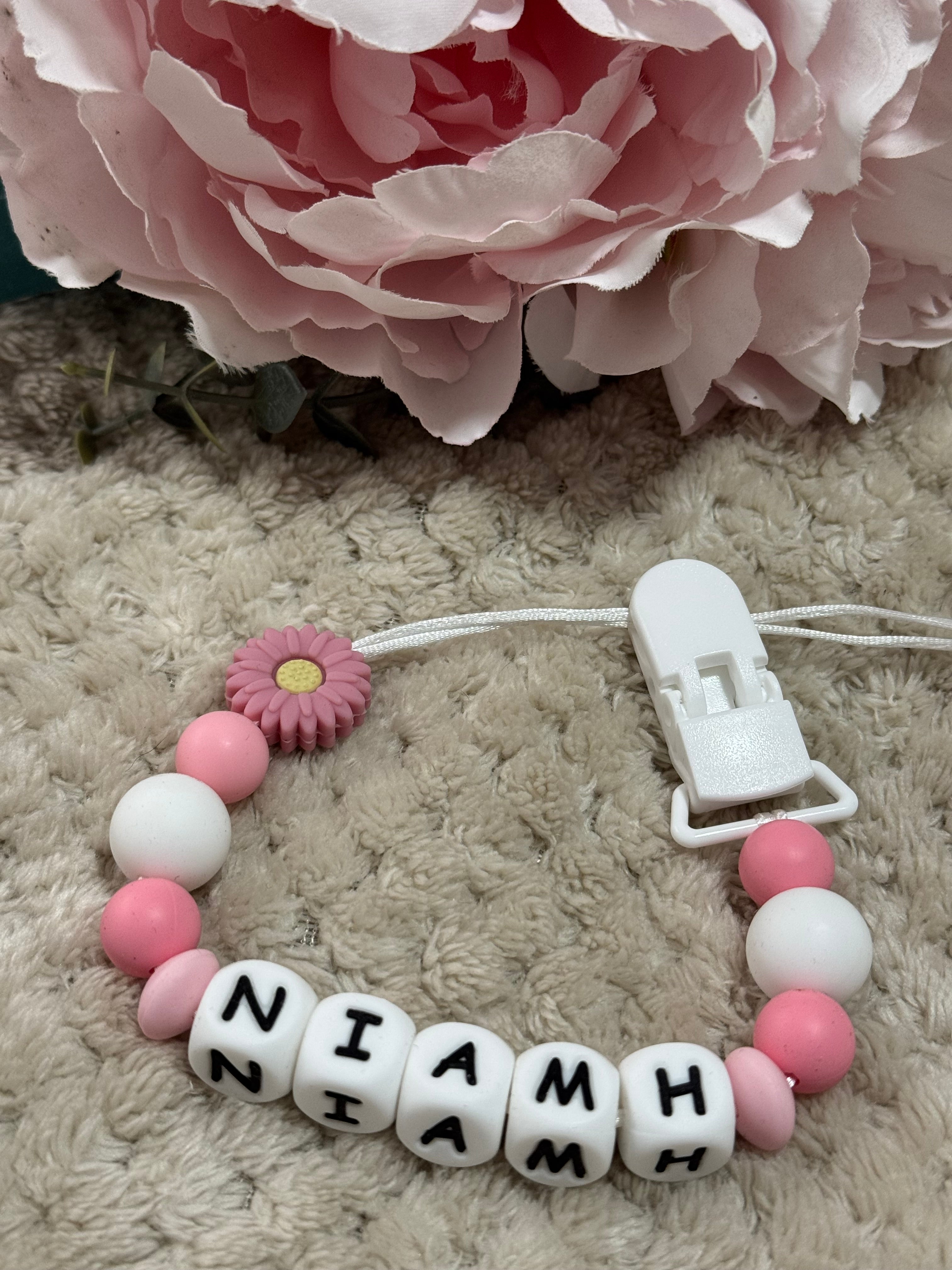 Baby teether with letter beads and pink flower on a textured surface