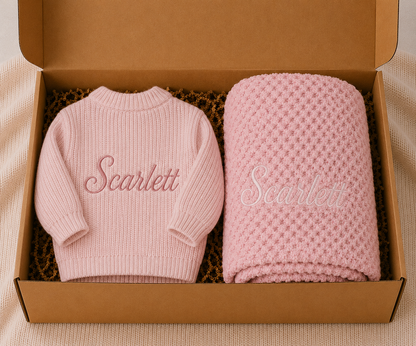 Pink baby sweater and blanket with 'Scarlett' embroidery in a cardboard box.