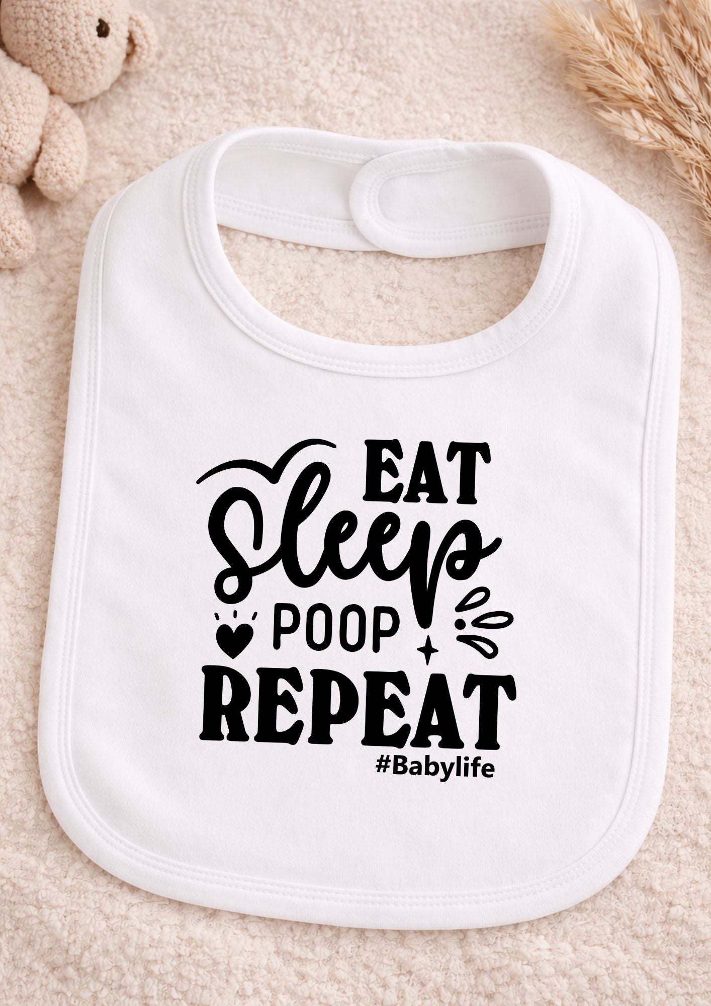 White baby bib with 'Eat Sleep Poop Repeat #Babylife' text on a beige background