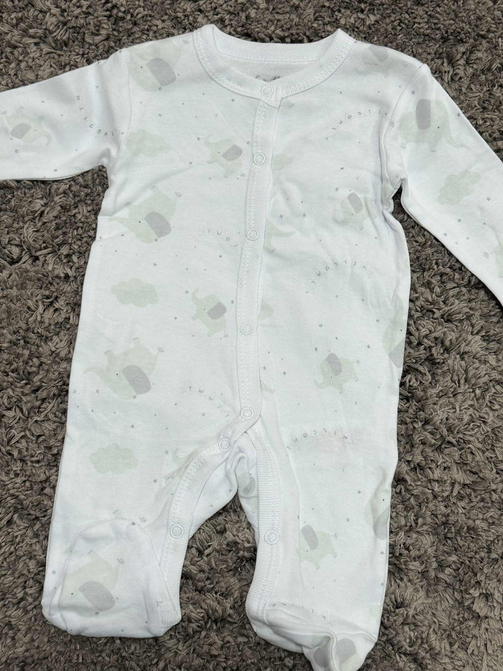 White baby onesie with gray patterns on a brown carpet