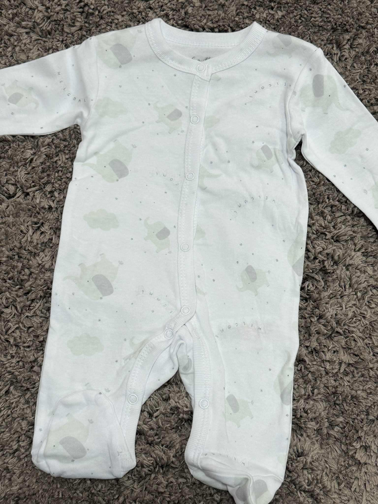 White baby onesie with gray patterns on a brown carpet
