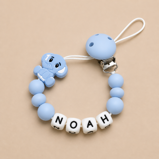 Baby dummy clip with elephant design and 'NOAH' beads on a beige background