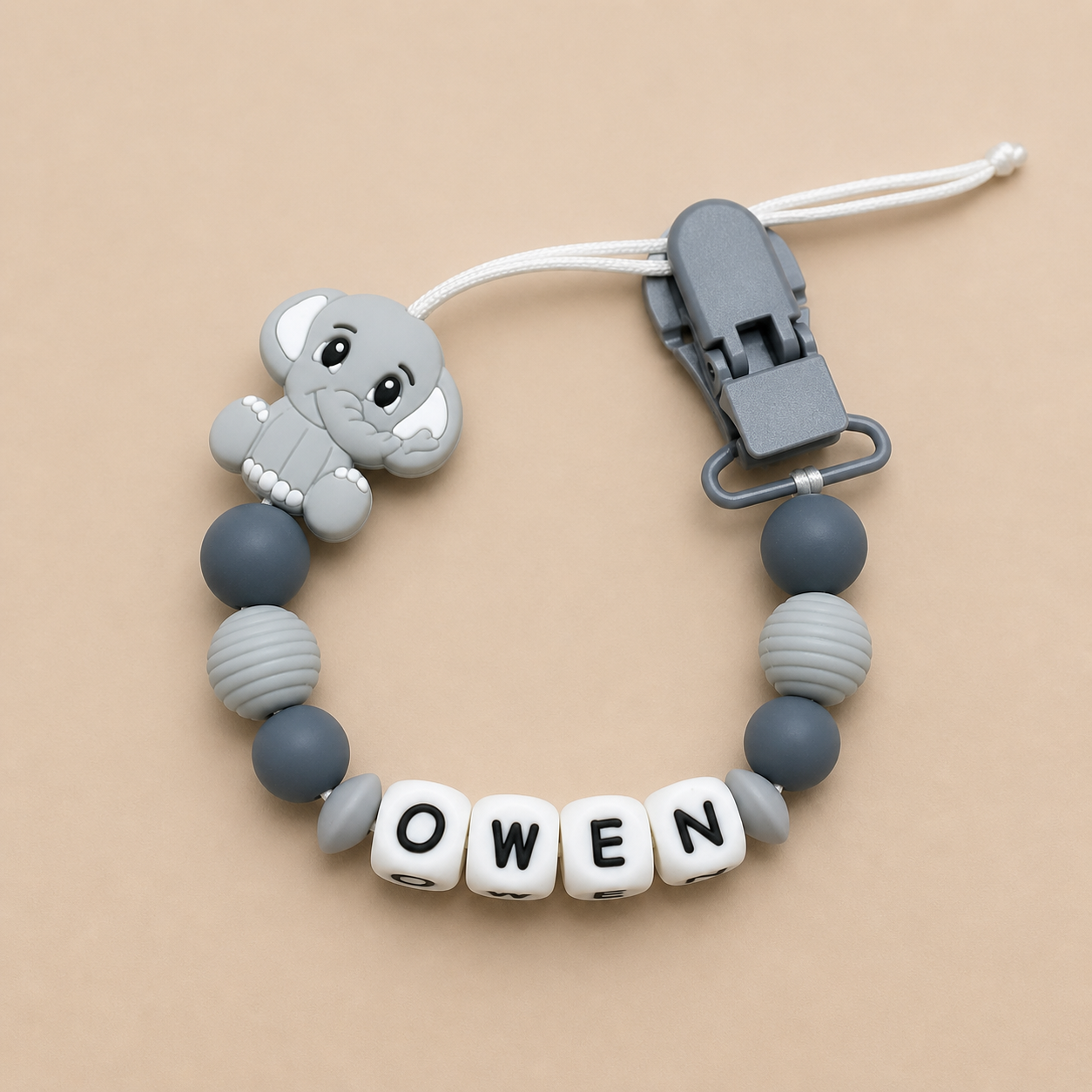 dummy clip with elephant charm and 'Owen' beads on a beige background