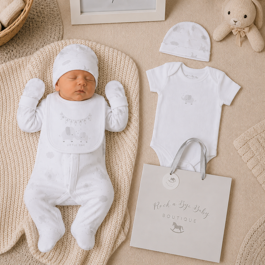 Newborn baby in white outfit with matching hat, baby onesie, and bag on a textured surface.