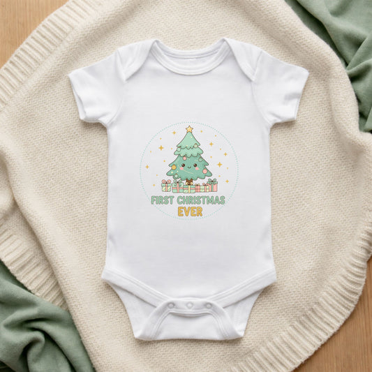 White baby onesie with a Christmas tree design and 'First Christmas Ever' text on a textured surface.