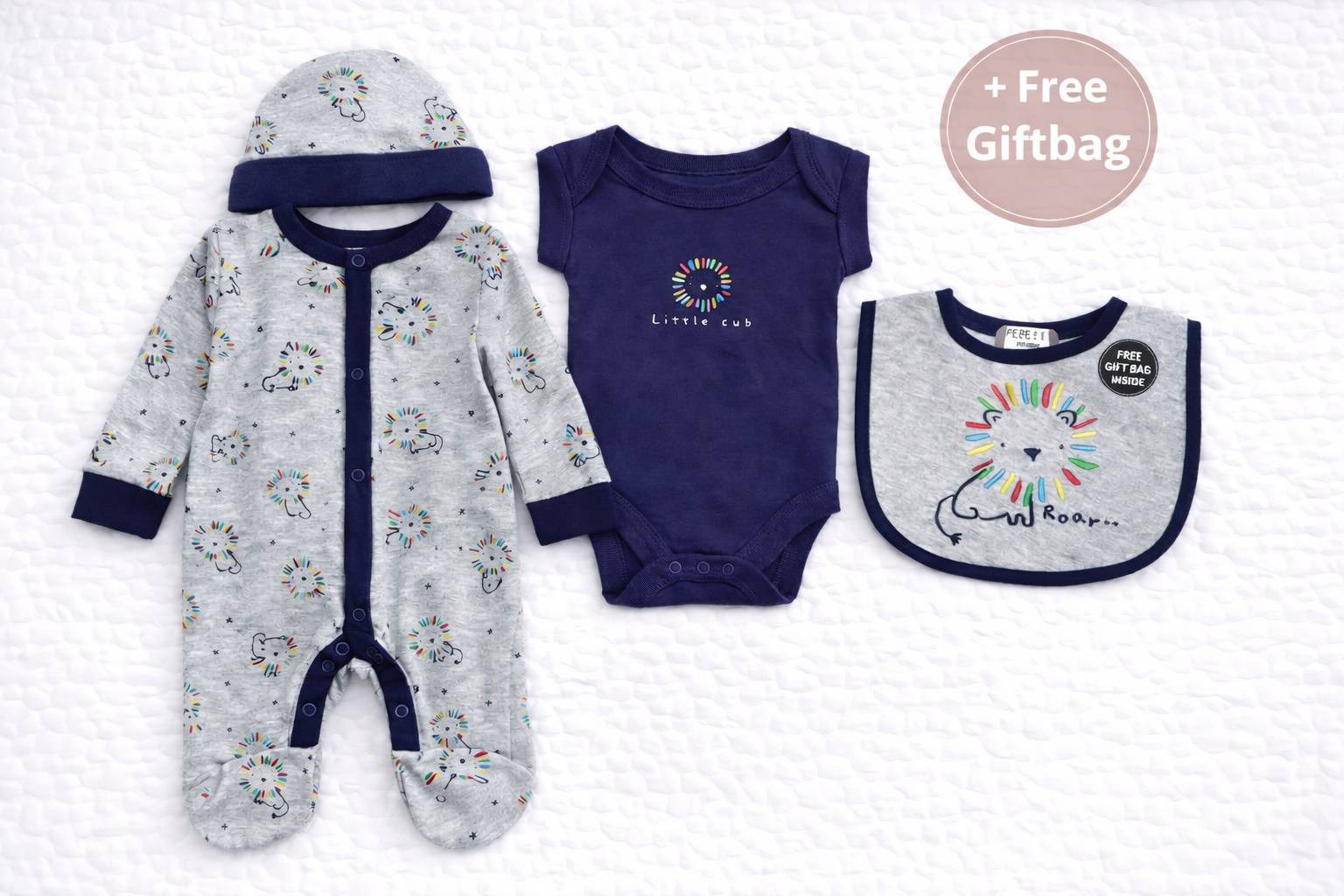 Flat lay mockup of a five-piece baby clothing set displayed on a white quilted background. The set includes a grey lion-print footed sleepsuit, matching hat, navy short-sleeve bodysuit with “Little Cub” print, and a coordinating lion bib. A circular “+ Free Giftbag” badge is shown in the top corner, highlighting the included gift bag.