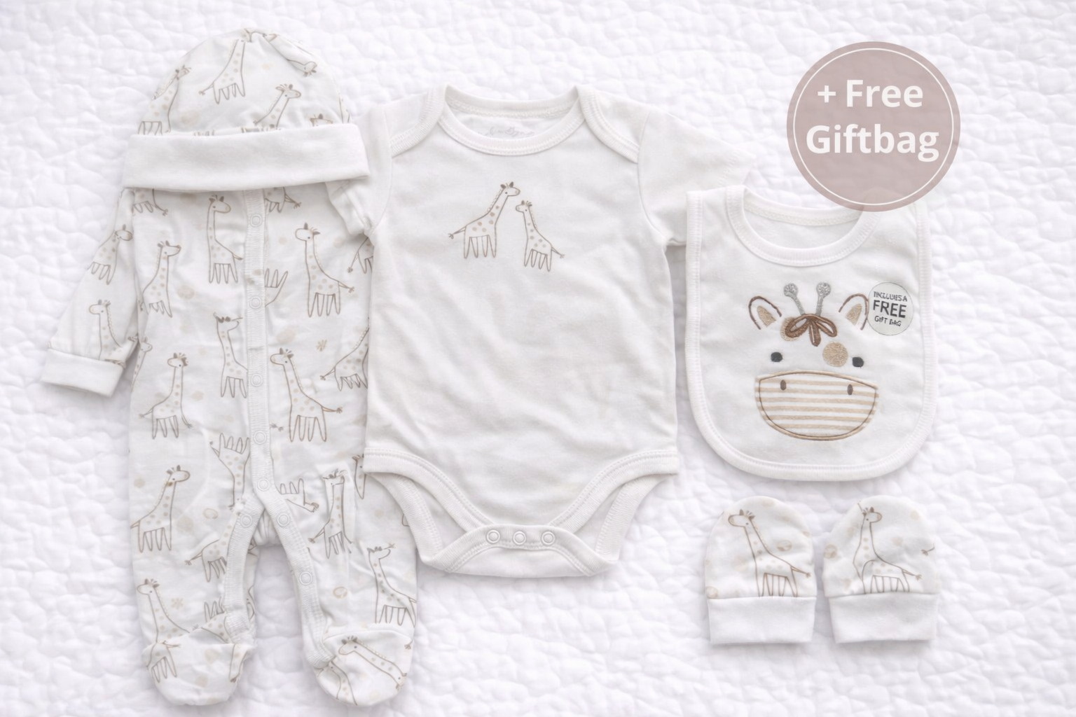 Five-piece newborn baby gift set featuring a soft giraffe print sleepsuit, matching short-sleeve bodysuit, coordinating hat, mittens, and embroidered giraffe bib. Displayed together with a circular “+ Free Giftbag” label, this neutral baby clothing set is perfect for newborns, baby showers, or gifting.