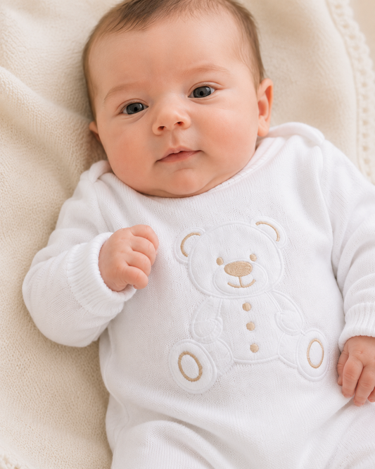 Baby wearing a white onesie with teddy bear design on a soft beige blanket