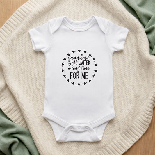 White baby onesie with text on a textured surface Grandma Has Waited a Long Time For Me Baby Vest