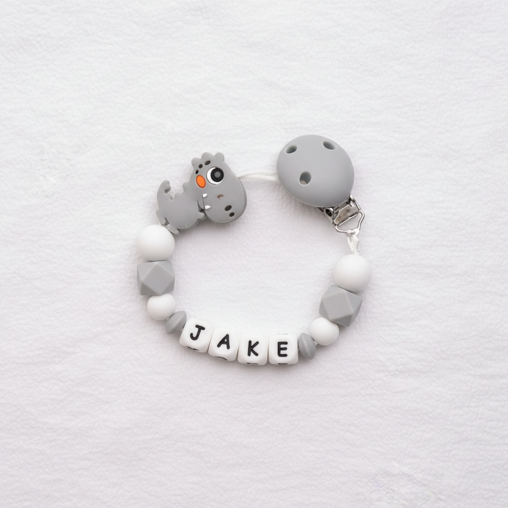 Personalised grey dinosaur dummy clip on a soft white luxury textured background.