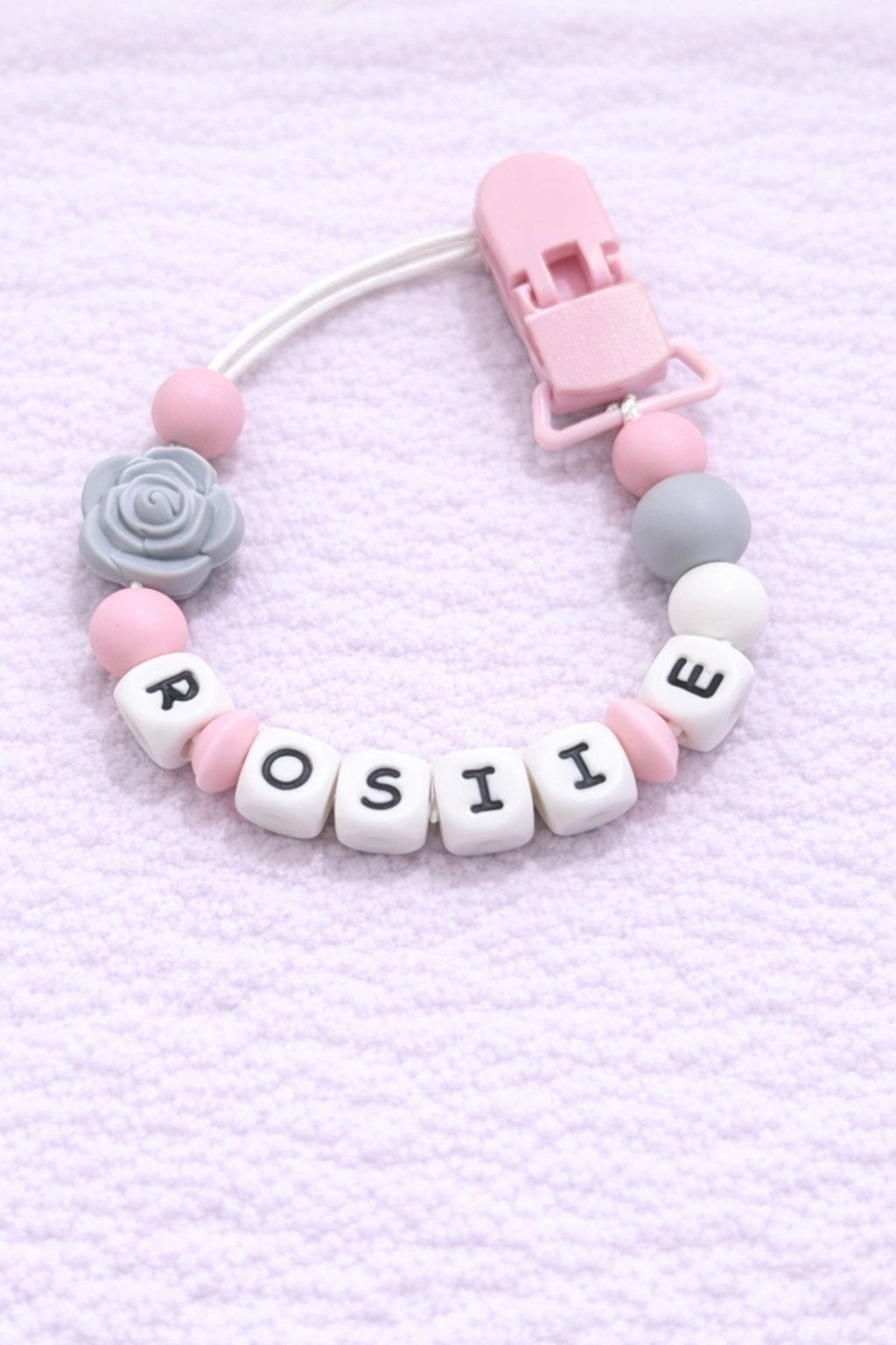Pastel-colored pacifier clip with 'ROSIE' on a light pink background