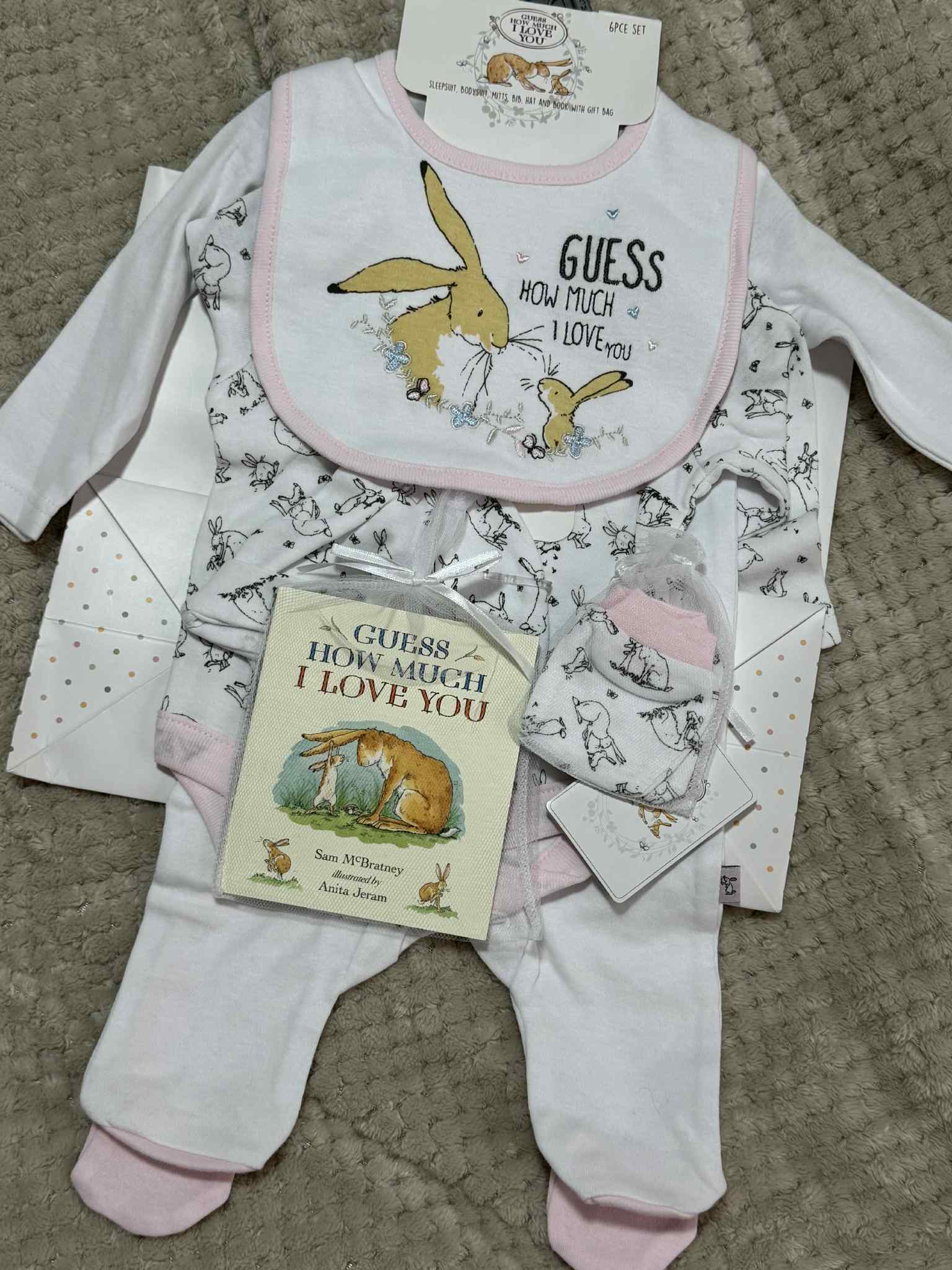 Baby clothing set with bib, pants, and book titled 'Guess How Much I Love You' on a textured surface.