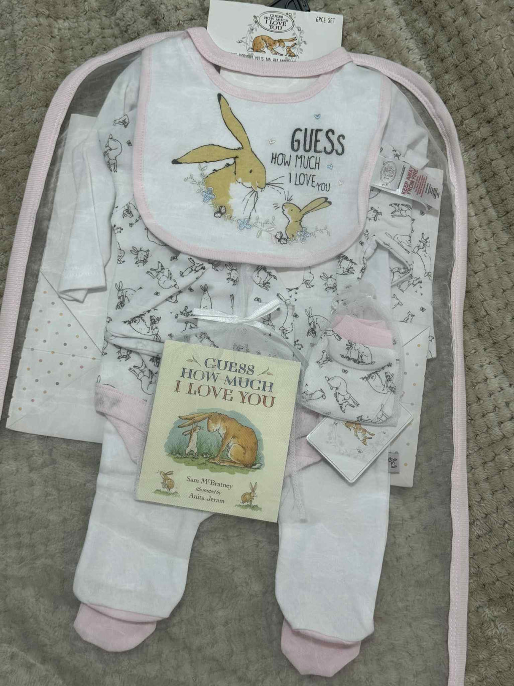 Baby clothing set with bib, onesie, and book on a textured surface