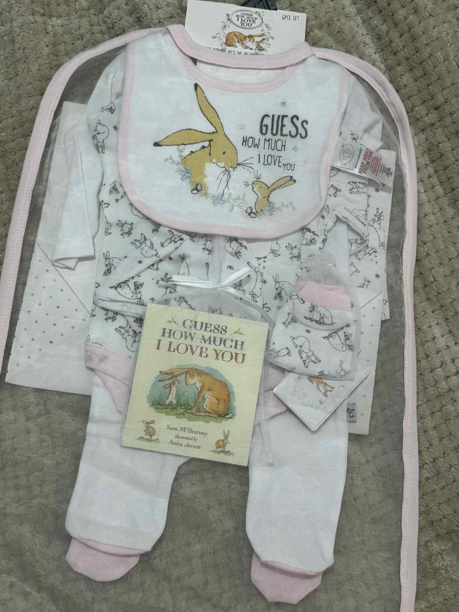 Baby clothing set with bib, onesie, and book on a textured surface