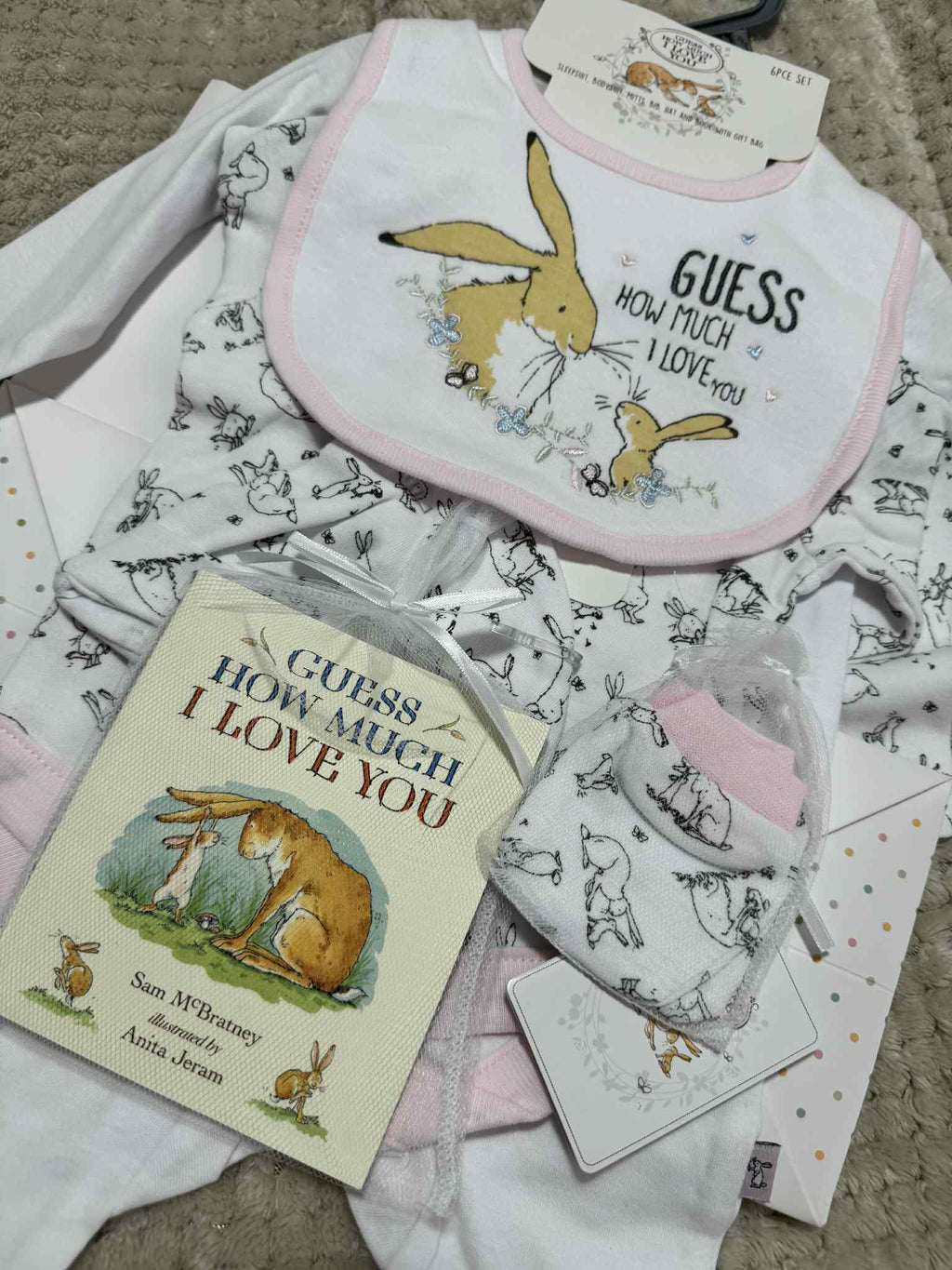 Baby bib, book, and blanket with 'Guess How Much I Love You' design on a textured surface.