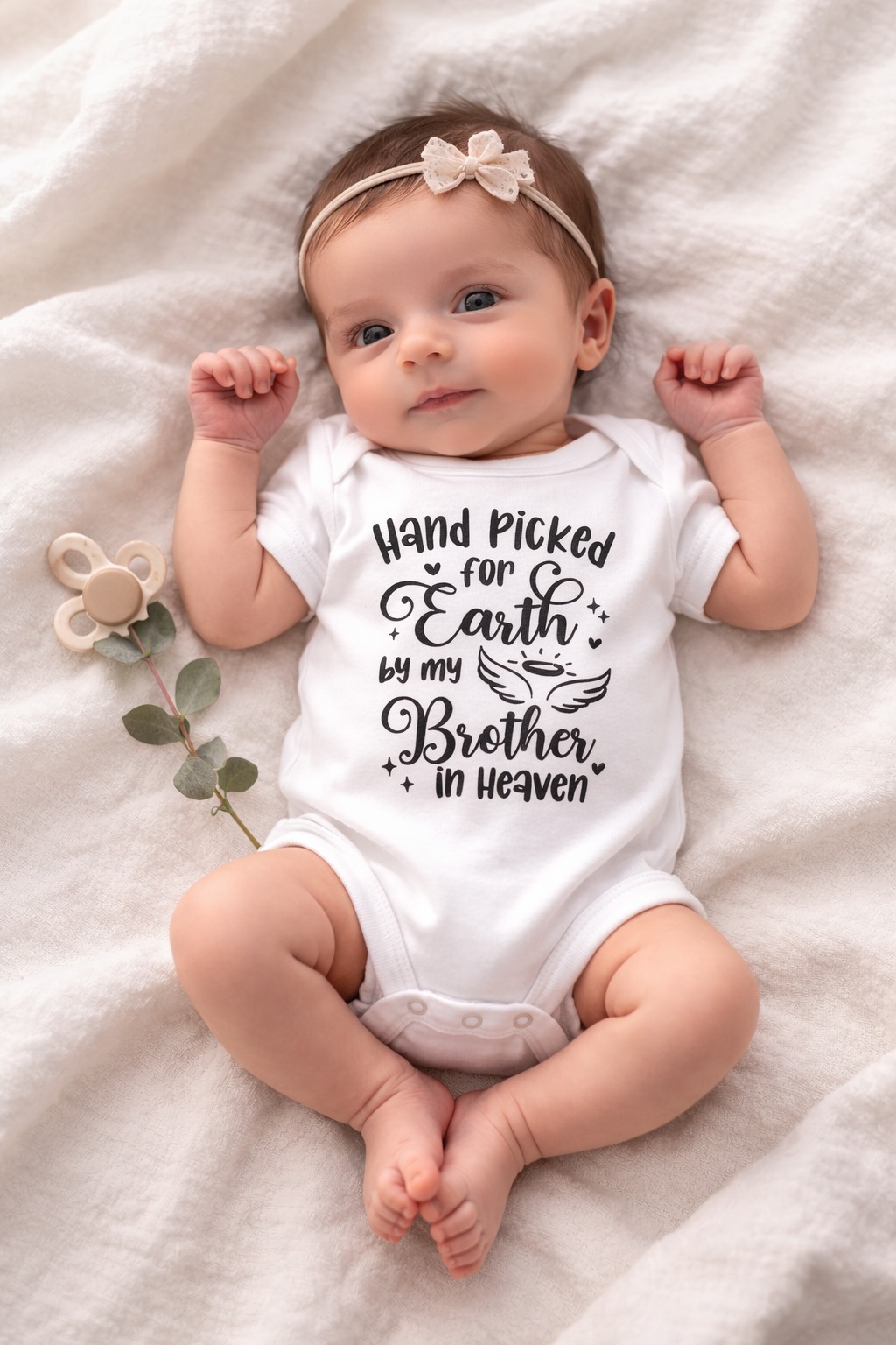 Baby wearing a white onesie with text, lying on a soft surface.