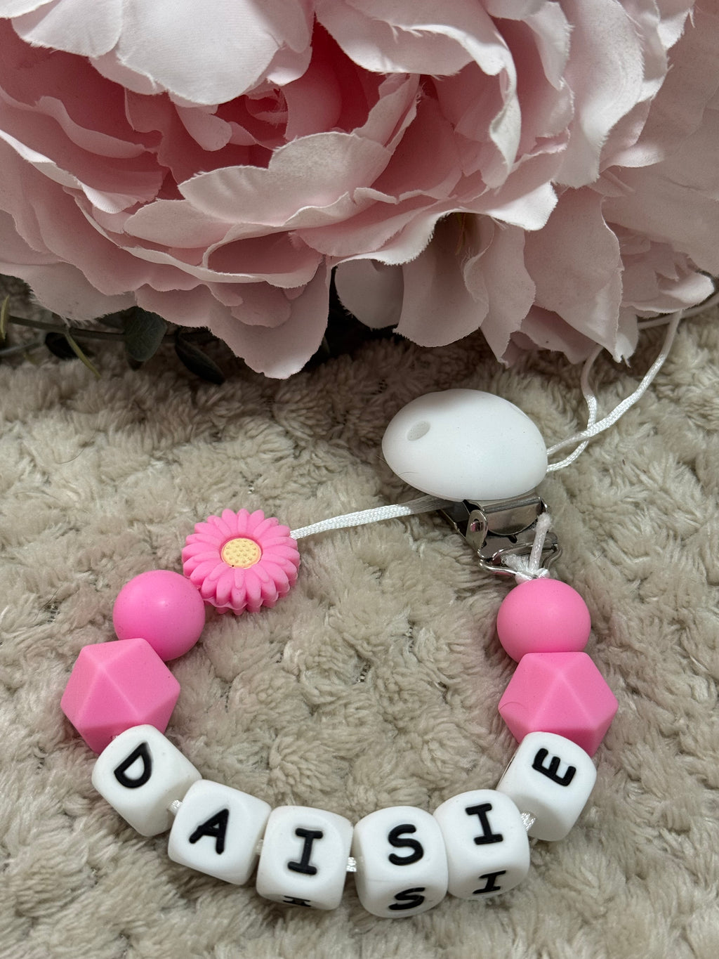 Baby Dummy Clip with pink and white beads and 'DAISIE' on a soft surface with pink flowers.