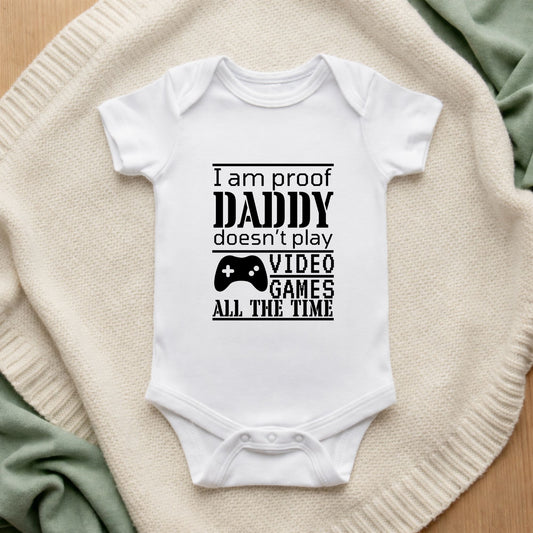 White baby onesie with text on a textured surface I Am Proof Daddy Doesn't Play Video Games All The Time Baby Vest