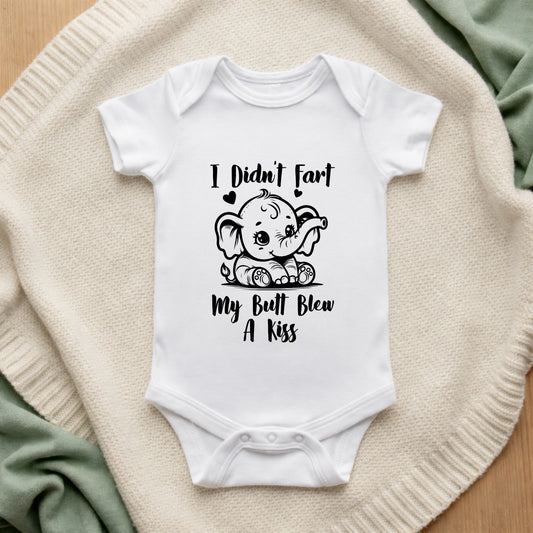 White baby onesie with humorous design and text on a textured surface.