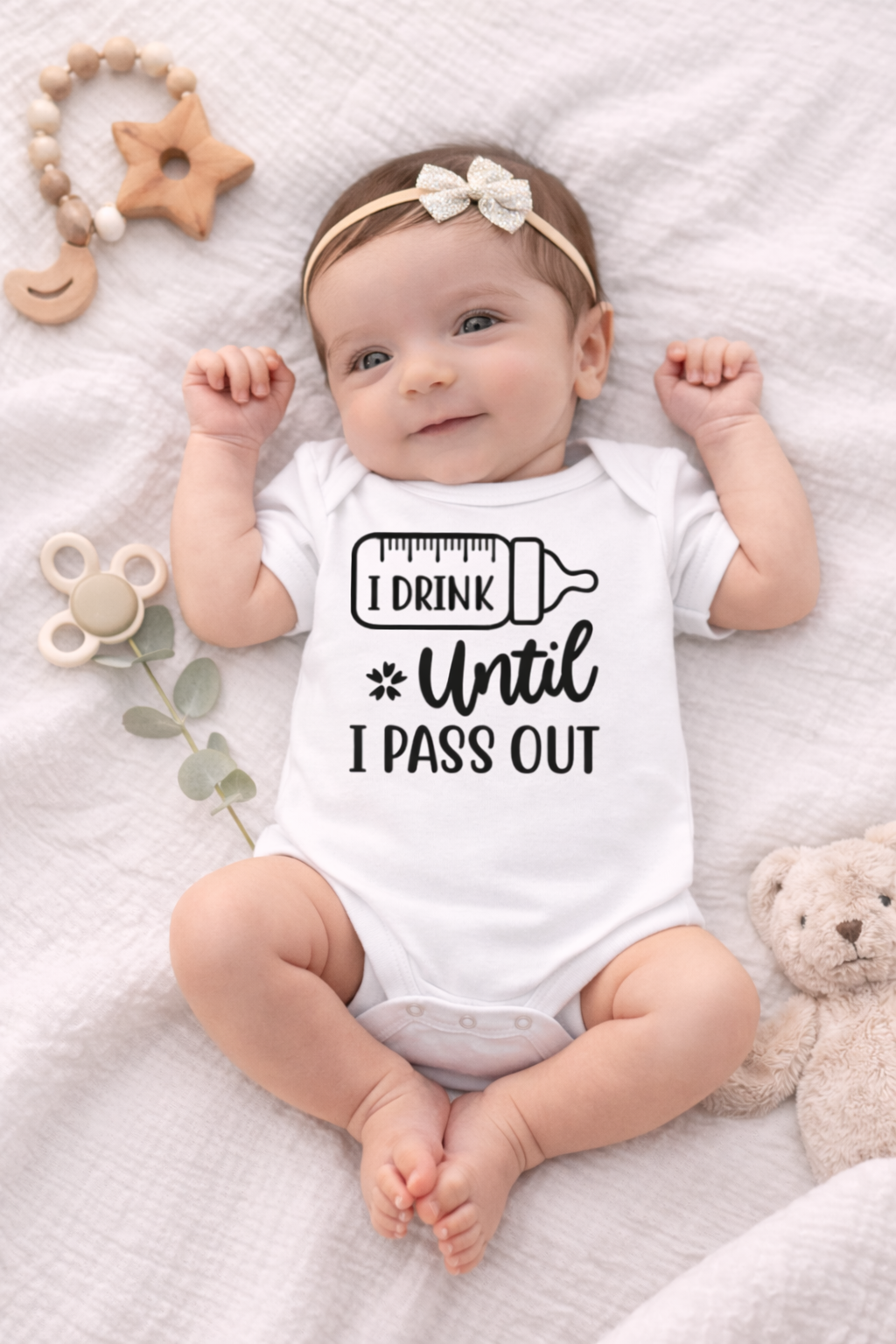 Baby wearing a white onesie with text, surrounded by toys on a soft surface