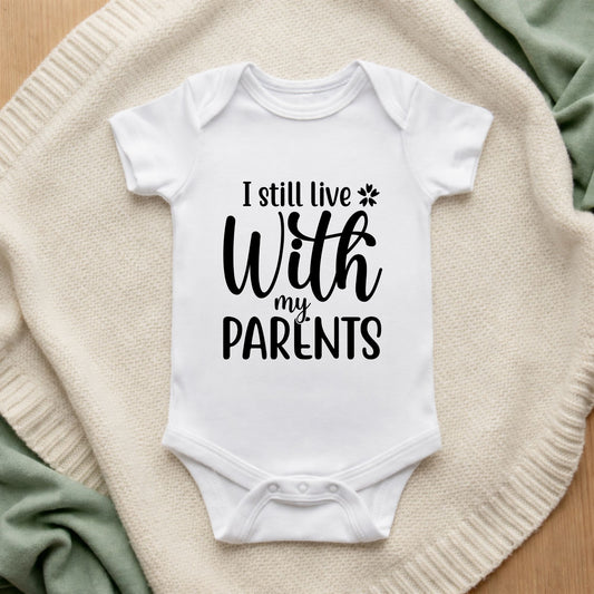 White baby onesie with text 'I still live with my parents' on a textured surface.