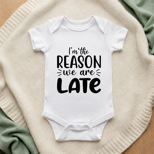 White baby onesie with text 'I'm the reason we are late' on a textured surface.