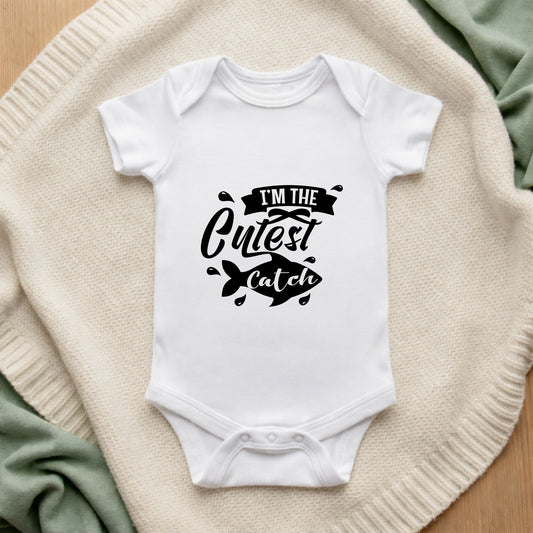 White baby onesie with black text on a textured surface I'm the Cutest Catch Baby Bodysuit