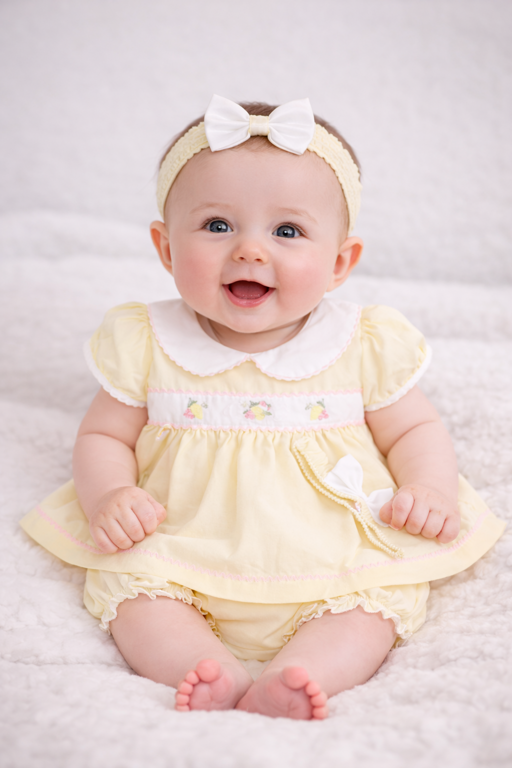 Baby wearing a yellow dress with a white collar and headband on a light background