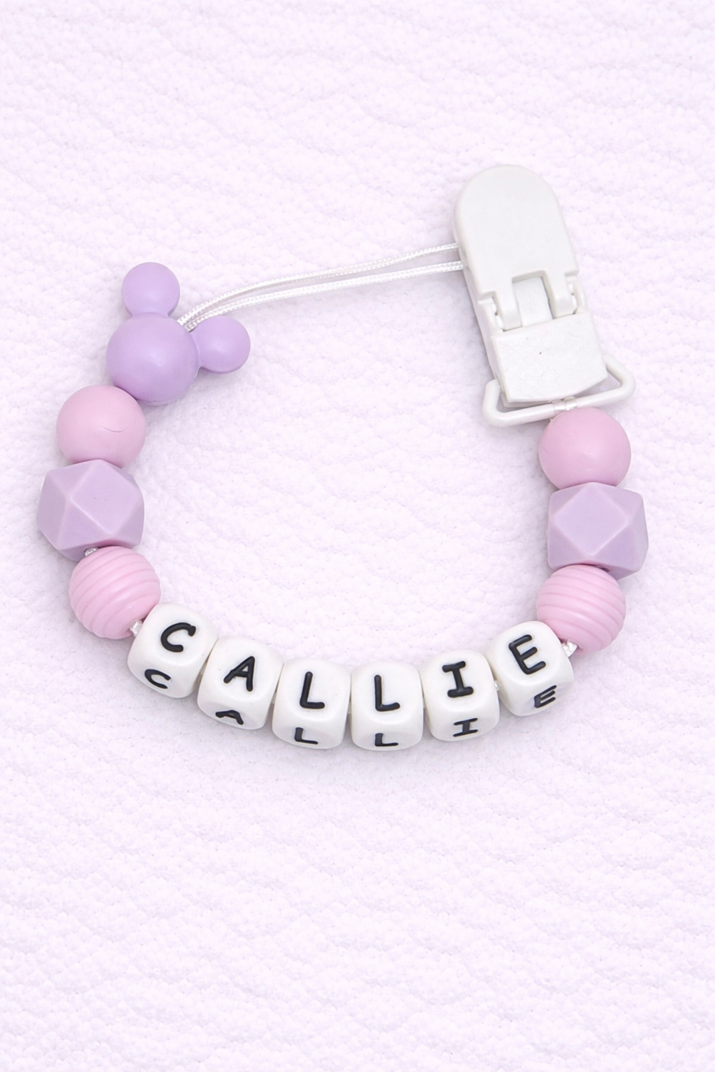 Dummy Clip with pink and purple beads and letter beads spelling 'CALLIE' on a light pink background