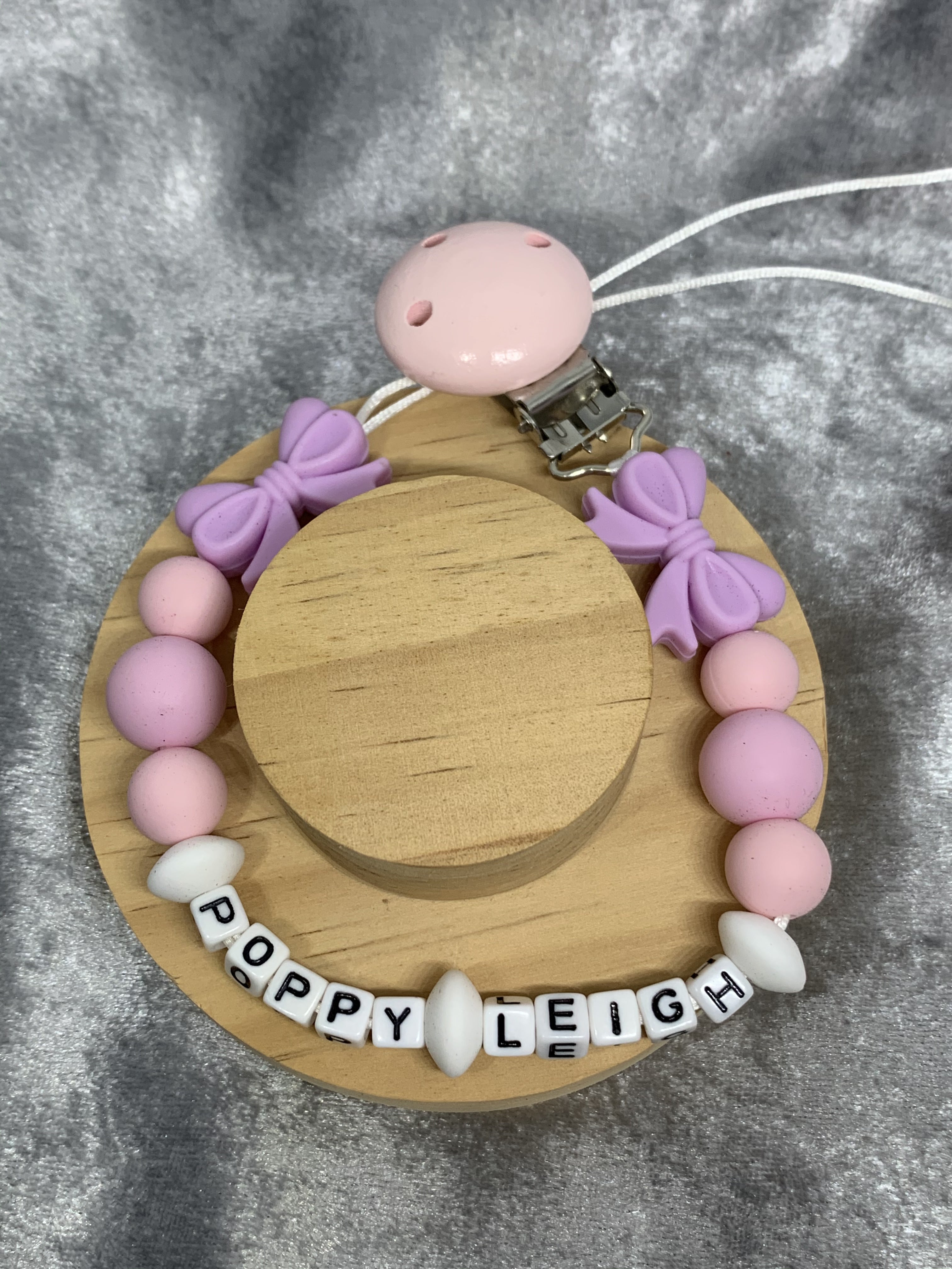 Pacifier clip with pink and purple beads and wooden disc on a gray background