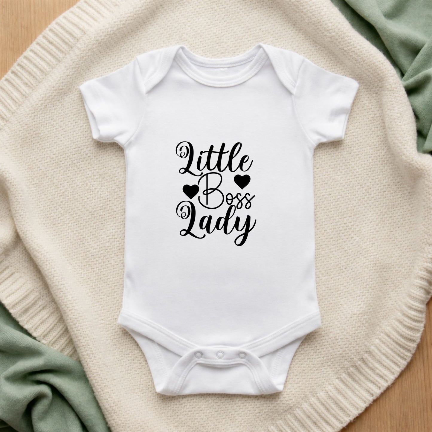 White baby onesie with 'Little Boss Lady' text on a textured surface