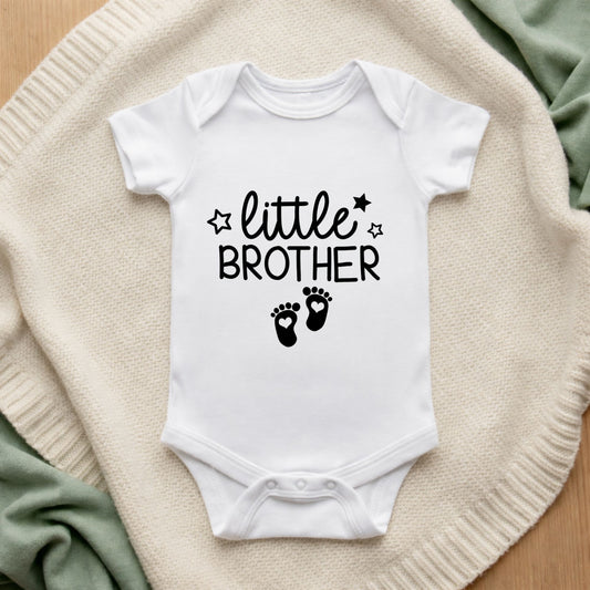 White baby onesie with 'little brother' text on a textured surface