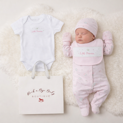 Baby girl's pink and white outfit with 'Little Princess' text, lying next to a baby bag on a soft surface.