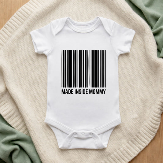 White baby onesie with a barcode and 'MADE INSIDE MOMMY' text on a textured surface.