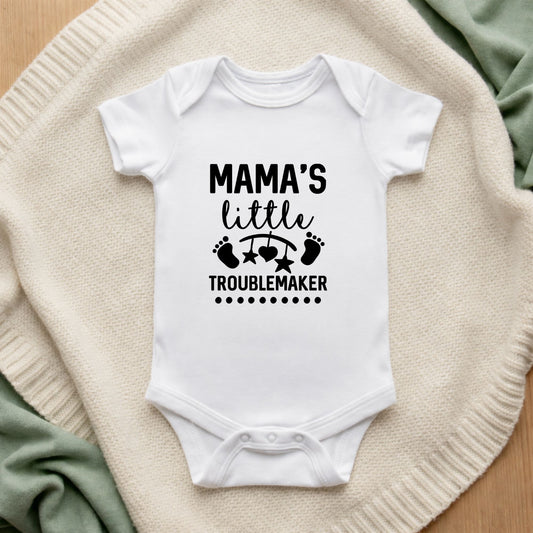 White baby onesie with 'Mama's Little Troublemaker' text on a textured surface