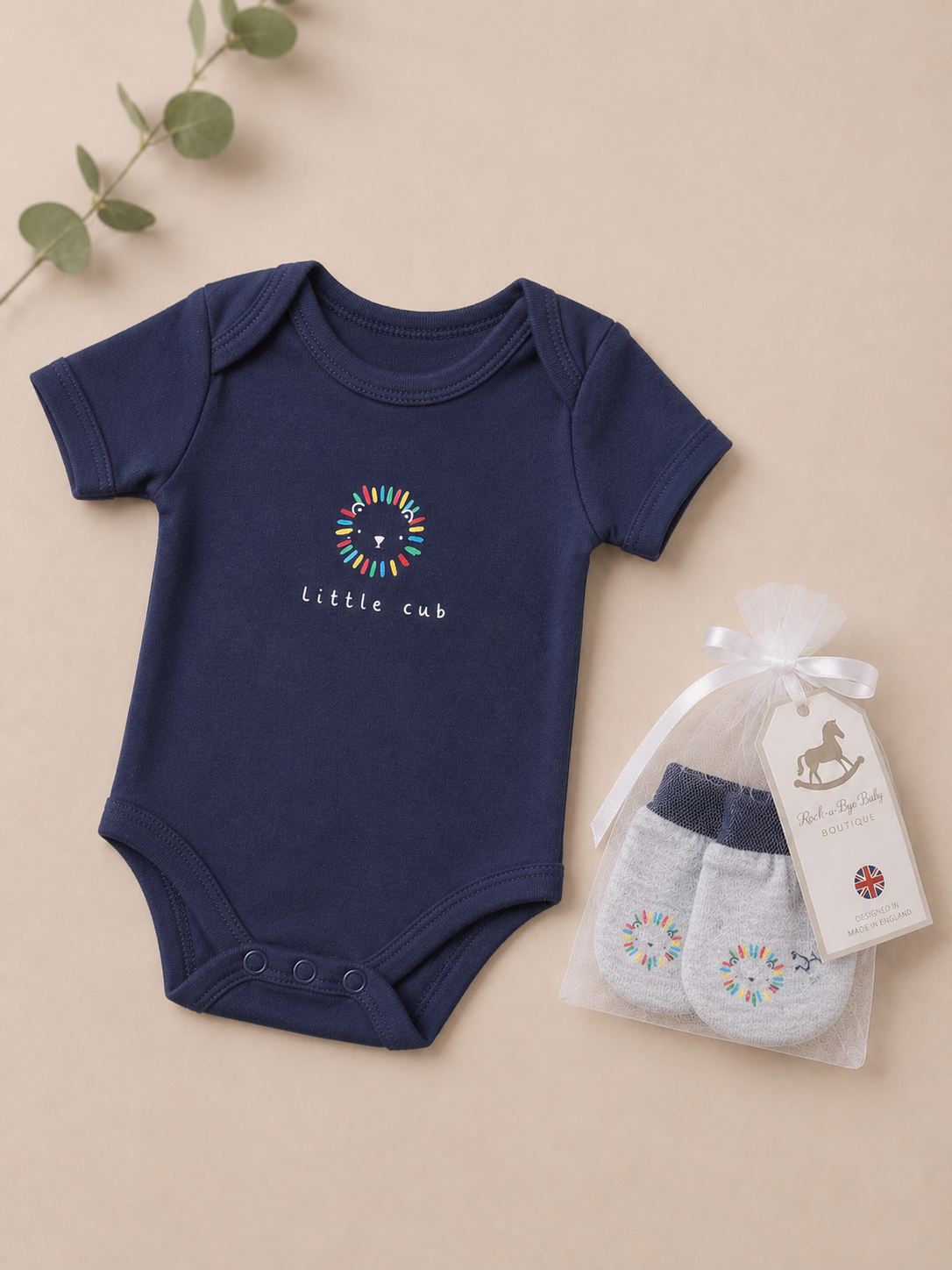 Navy blue baby bodysuit with 'little cub' design and gray mittens in a bag on a beige background.