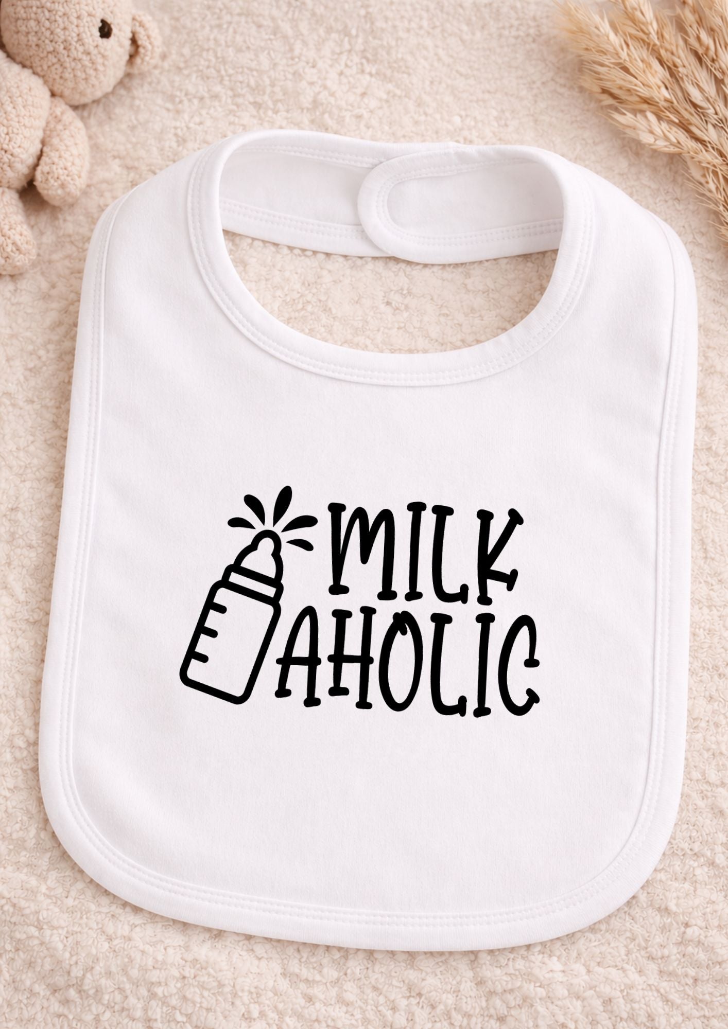White baby bib with 'Milk Aholic' text on a beige surface