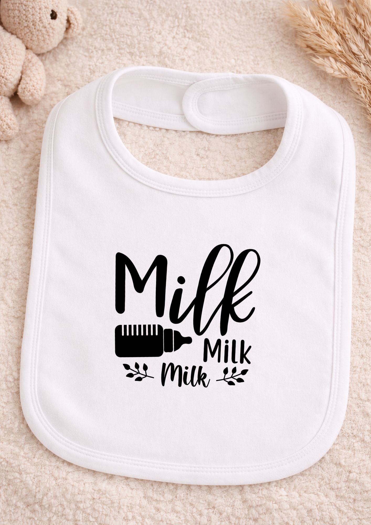 White baby bib with 'Milk Milk Milk' text on a beige surface