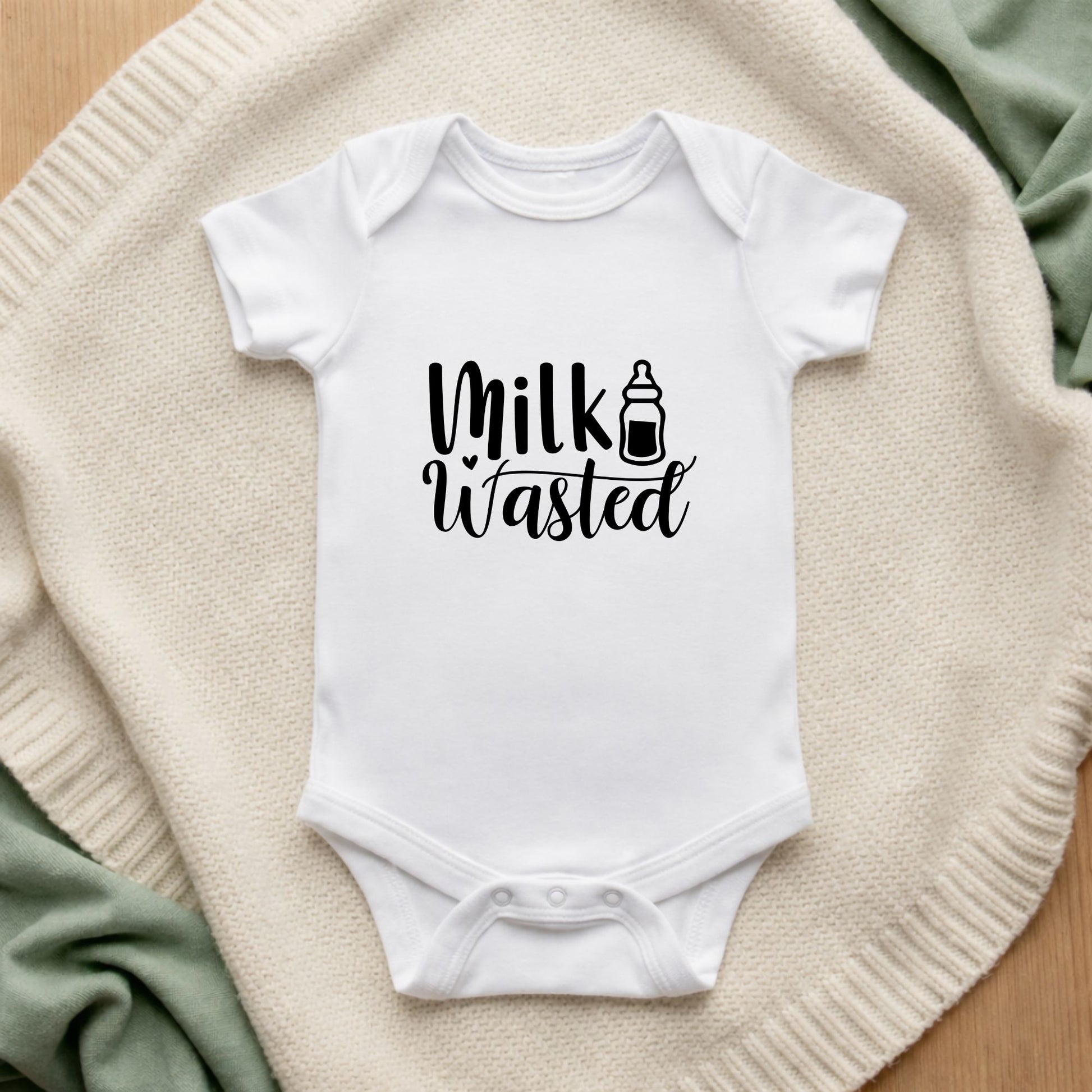 White baby onesie with 'Milk Wasted' text on a textured surface
