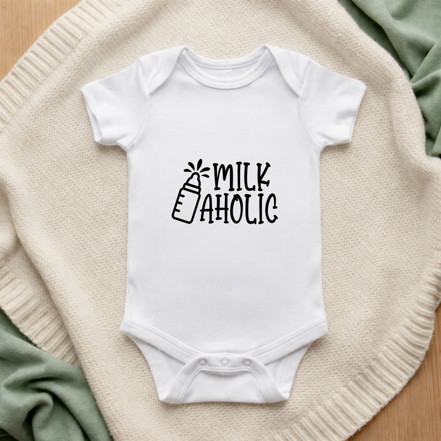 White baby onesie with 'Milk Aholic' text on a textured surface