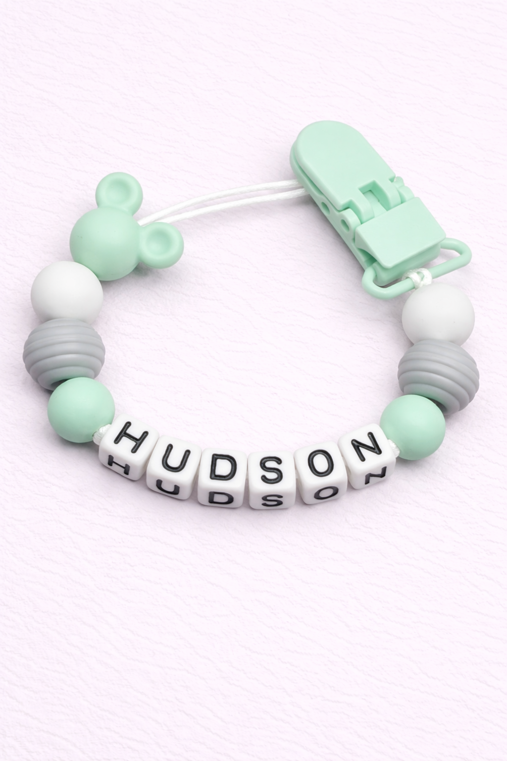 Mint and gray teething dummy clip with 'Hudson' on a white background