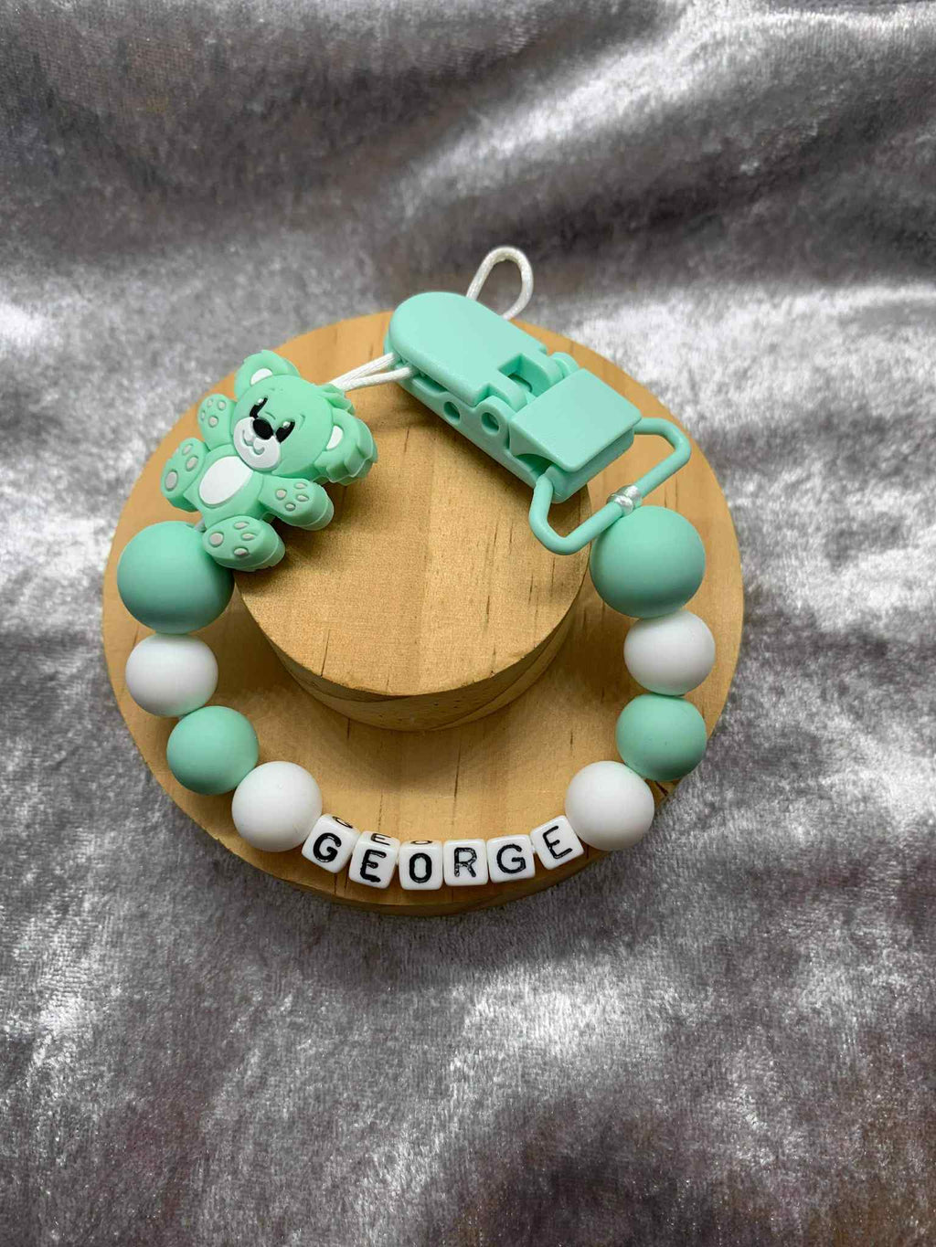 Mint Green and white teddybear dummy chain on a grey textured surface personalised with the name ''George'. Personalisation and MAM Adapter options available.