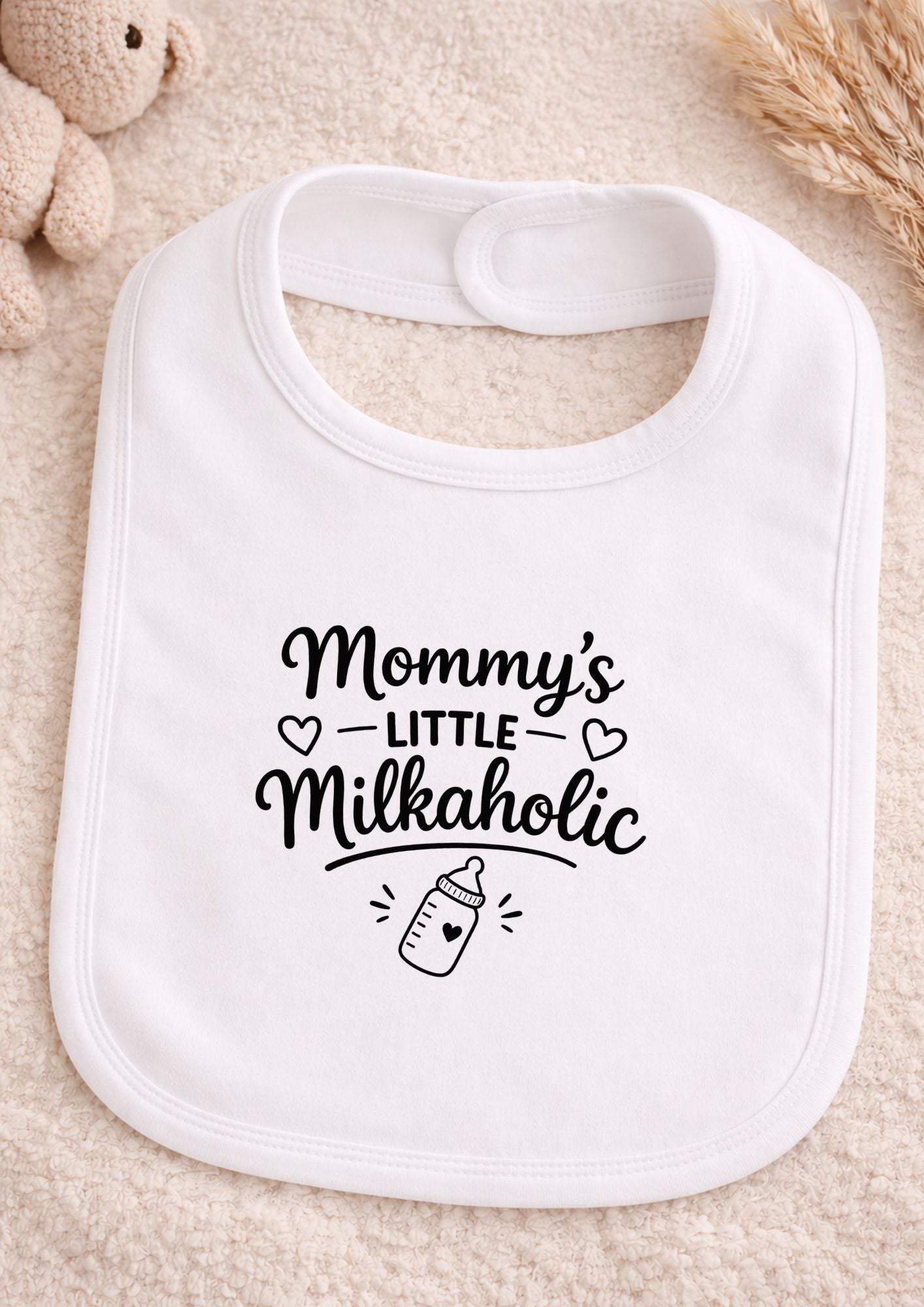 White bib with 'Mommy's Little Milkaholic' text on a beige surface
