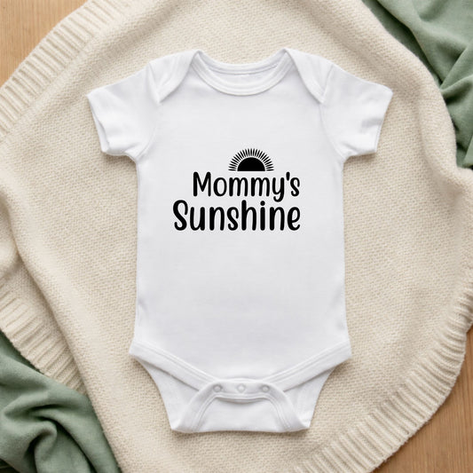 White baby onesie with 'Mommy's Sunshine' text on a textured surface