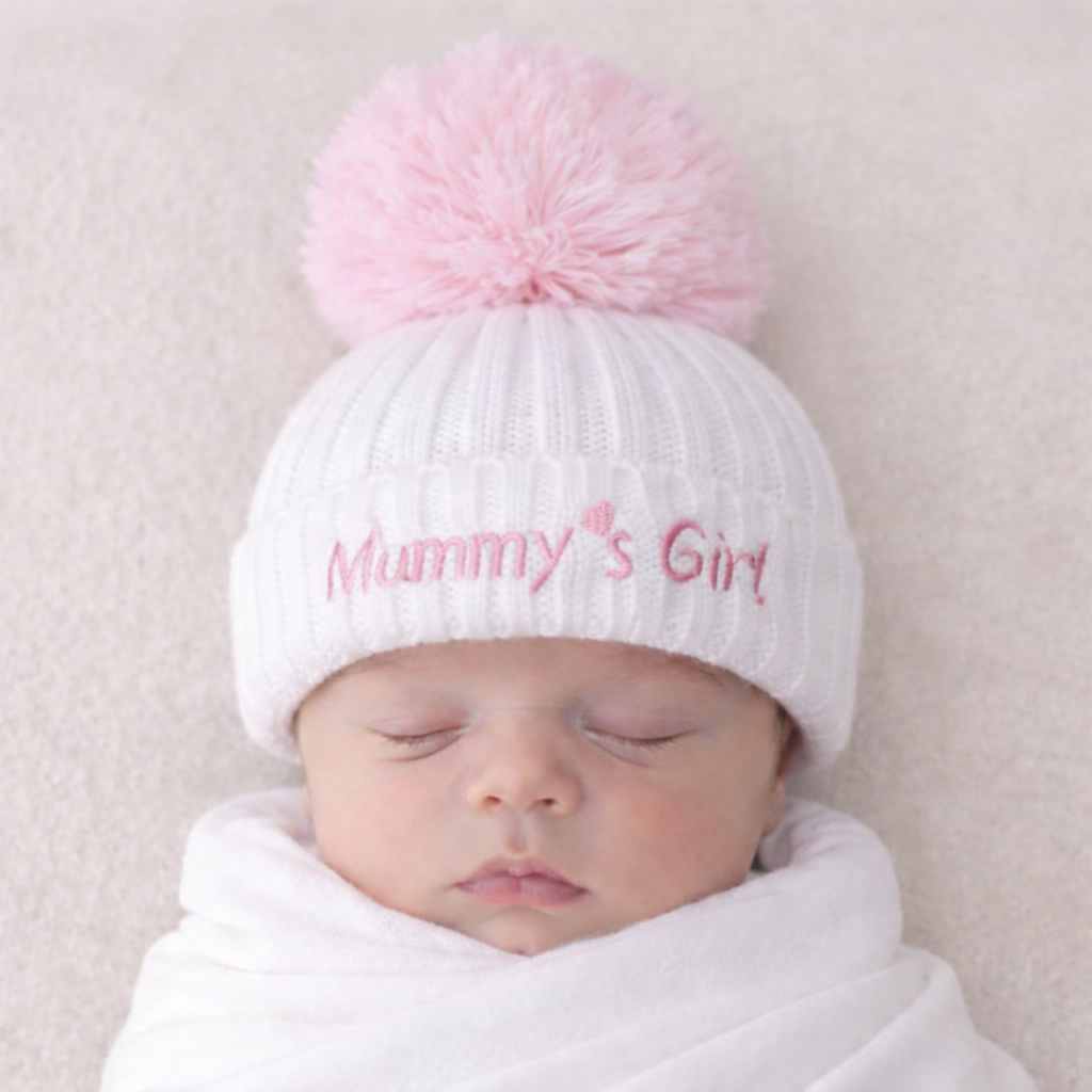 Newborn baby wearing a white knit hat with a pink pom-pom and 'Mummy's Girl' text on a neutral background.