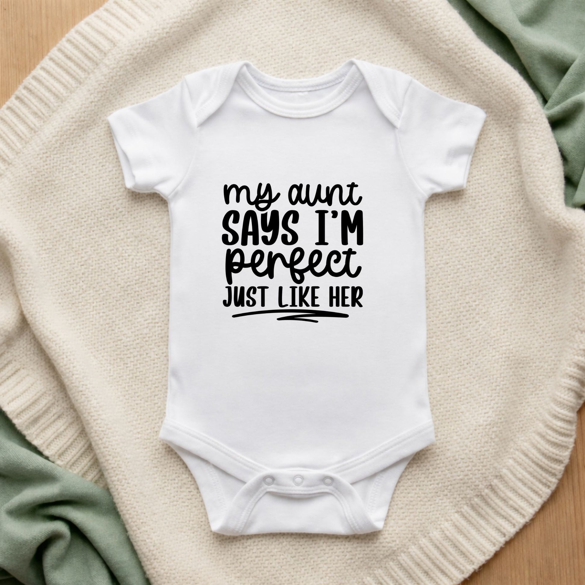 White baby onesie with text on a textured surface My Aunt Says I'm Perfect Just Like Her Baby Vest