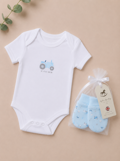 White baby bodysuit with blue tractor design and a set of blue baby socks on a beige background.