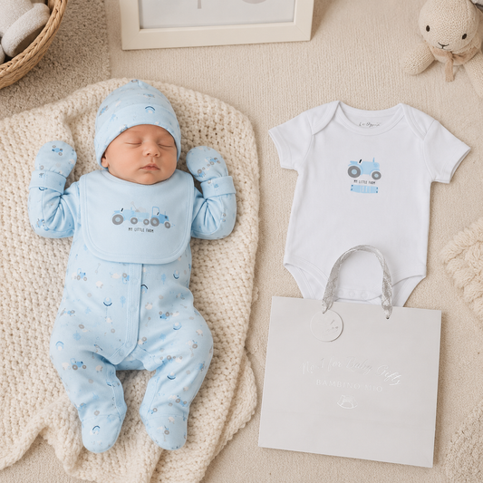 Newborn baby in blue outfit with matching hat and matching onesie on a beige blanket.