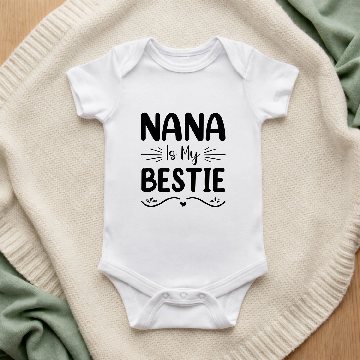White baby onesie with 'Nana is my bestie' text on a soft fabric background