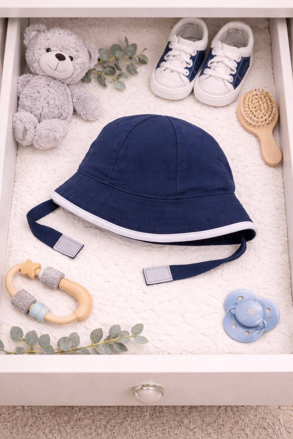 Baby items including a navy hat, shoes, teether, pacifier, and teddy bear in a drawer.
